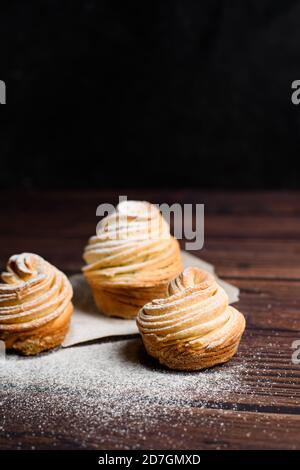 le moderne cruffine sono realizzate con croissant in puff sotto forma di muffin, su fondo scuro in zucchero in polvere. Copia spazio. La vista dall'alto. clos Foto Stock