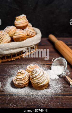 le moderne cruffine sono realizzate con cornetti di puff sotto forma di muffin, in un cesto di legno su fondo scuro, cosparso di zucchero in polvere. Copia sp Foto Stock