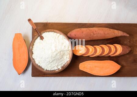 farina di patate dolci in un piatto di legno. le patate dolci sono un ingrediente organico vegano per un'alimentazione sana su uno sfondo chiaro Foto Stock