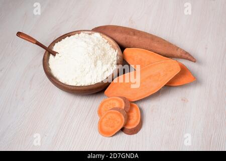 farina di patate dolci in un piatto di legno. le patate dolci sono un ingrediente organico vegano per un'alimentazione sana su uno sfondo chiaro Foto Stock