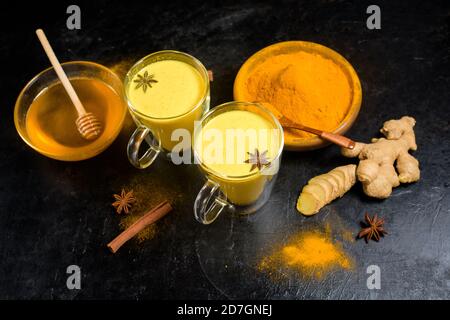 Latte tradizionale indiano dorato con curcuma, zenzero, spezie, miele. In bicchieri di vetro trasparente. Effetto curativo della bevanda. Ingredienti per una dri dorata Foto Stock