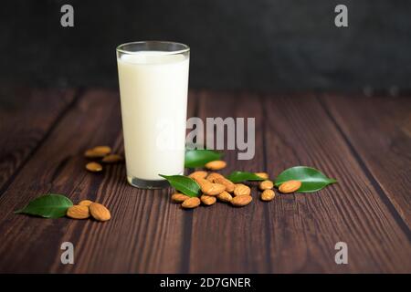 latte di mandorle in un bicchiere su fondo di legno. primo piano di semi di mandorle e foglie verdi accanto al bicchiere. Foto Stock