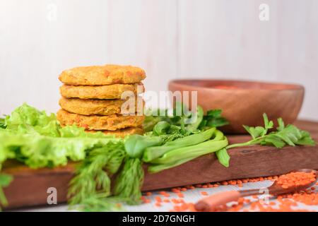 tagliole vegetariane da lenticchie e carote in un piatto di legno con verdure ed erbe. cibo sano. lenticchie rosse in un piatto di legno su un backgr leggero Foto Stock