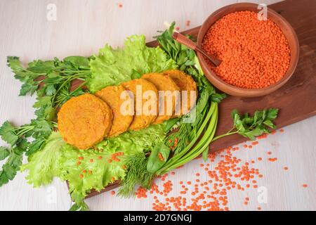 tagliole vegetariane da lenticchie e carote in un piatto di legno con verdure ed erbe. cibo sano. lenticchie rosse in un piatto di legno su un backgr leggero Foto Stock