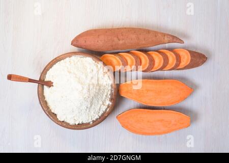 farina di patate dolci in un piatto di legno su sfondo chiaro. patate dolci fresche tagliate a pezzi d'arancia accanto alla farina. vista dall'alto. clo Foto Stock