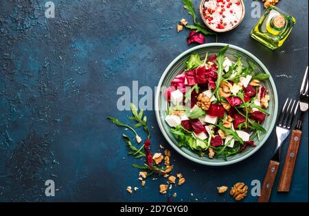 Insalata estiva di barbabietole con rucola, radicchio, formaggio morbido e noci su piatto con forchetta, condimento e spezie su tavolo da cucina blu, spazio copia, vista dall'alto Foto Stock