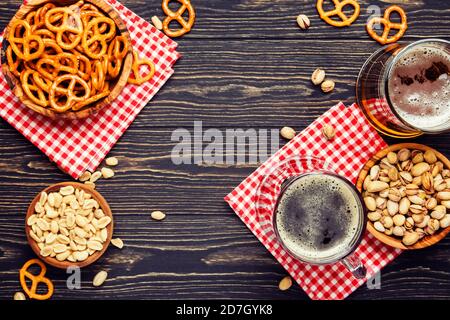 Birra tedesca chiara e scura in grandi tazze e ciotole con spuntini e noci salati, concetto di festival della birra d'autunno, tavolo di legno scuro, vista dall'alto Foto Stock