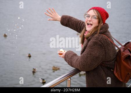 Donna felice che alimenta anatre sul laghetto invernale Foto Stock