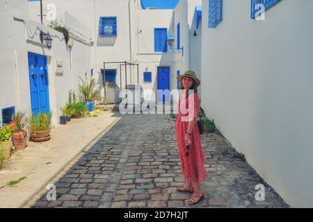 Una giovane donna si trova nel cortile con finestre blu e porte con ornamenti arabi. Tessitura dei simboli islamici in Sidi Bou Said, Tunisia, Africa Foto Stock