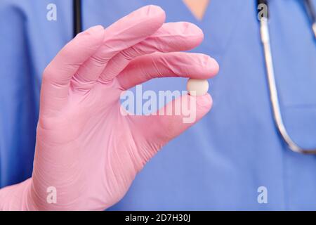 Mano in un guanto medico contiene una pillola bianca, primo piano Foto Stock