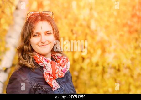 Ritratto autunnale di una ragazza in piedi nelle foglie di un albero. Una giovane donna sta in piedi da vicino ai rami di un salice piangente. Giorno di sole, giallo Foto Stock