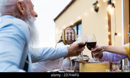 Felici anziani multirazziali che tostano insieme con bicchieri di vino rosso Cena nel patio della casa - concetto di gente anziana di stile di vita Foto Stock