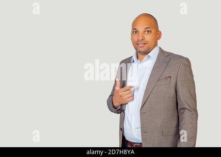 Ritratto del giovane uomo d'affari afro-americano che punta con il dito indice alla macchina fotografica e sorridente luminoso. In piedi su uno sfondo grigio Foto Stock