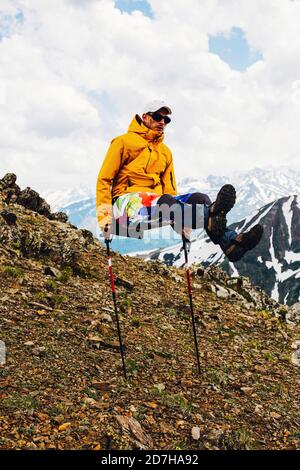 Giovane felice arrampicatore maschio sta tenendo le sue due mani su bastoni con le gambe allungate in avanti. Concetto di umorismo nella campagna Foto Stock