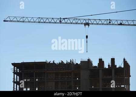 Sagome di lavoratori sul cantiere di un alto costruzione contro il cielo blu Foto Stock