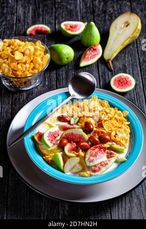 Sana colazione del mattino: Ciotola blu con yogurt naturale con fiocchi di mais croccanti, fichi, pera serviti su sfondo di legno nero, vista dall'alto, clos Foto Stock