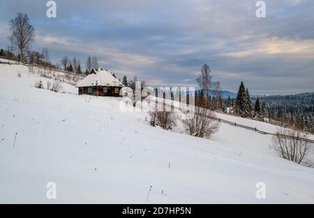 Colline di campagna, boschetti e terreni agricoli in inverno remoto villaggio di montagna alpina, e piccola vecchia casa abbandonata sulla collina Foto Stock