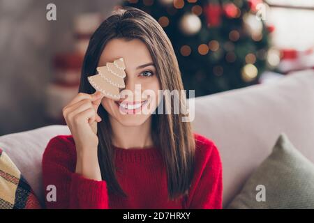 Ritratto di occhi di copertura ragazza positivi con x-mas gustoso zenzero il biscotto di pane siede il divano in casa all'interno Foto Stock