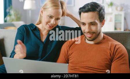Felice bella coppia siede su un divano a casa, il ragazzo tiene, navigare attraverso Internet, fare e-Shopping, utilizzando i servizi di streaming. Felice famiglia dentro Foto Stock