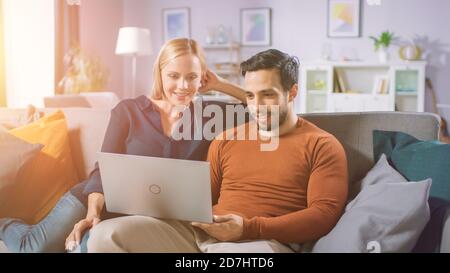 Felice bella coppia siede su un divano a casa, il ragazzo tiene, navigare attraverso Internet, fare e-Shopping, utilizzando i servizi di streaming. Felice famiglia dentro Foto Stock