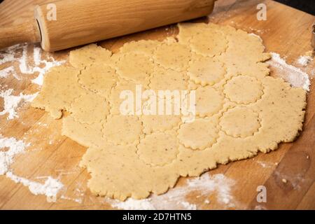 Panetteria di Natale: Pasta di biscotto (Shortcrust) rotolato fuori su una tavola di cucina di legno sulla farina. Perno di rotolamento visibile. Biscotti arrotondati tagliati. Messa a fuoco selettiva Foto Stock