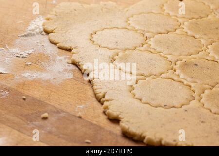 Cottura di Natale: Pasta di biscotti (Shortcrust) arrotolata su una piastra di legno da cucina sulla farina. Biscotti arrotondati tagliati. Foto Stock