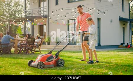 Il buon Padre insegna a Son come usare camminare dietro il tosaerba, lo spingono insieme, tagliando l'erba. La famiglia trascorre il proprio tempo insieme in un giorno di sole. Foto Stock