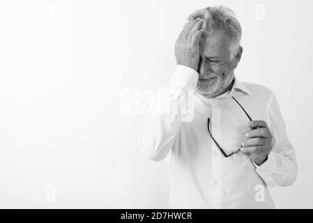 Studio shot di sad senior uomo barbuto tergi le lacrime mentre si tiene un occhiale contro uno sfondo bianco Foto Stock