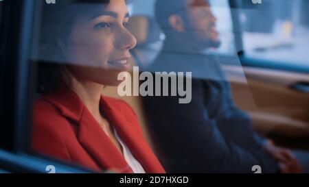 Bella donna e il suo maschio Partner Riding nella sede posteriore di un'auto. È sera nella Big City. Camera Shot dall'esterno del veicolo. Foto Stock