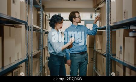 Inventario femminile Gestione e Storage Worker, verifica delle scorte e discussione sul lavoro. Nelle file di sfondo di scaffali pieni di pacchi con prodotti Foto Stock