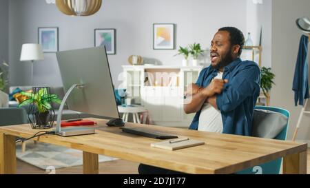 Ritratto dello scioccato bell'uomo afro-americano seduto sul suo posto di lavoro. Giovane uomo che guarda gli Screamers a casa. Foto Stock