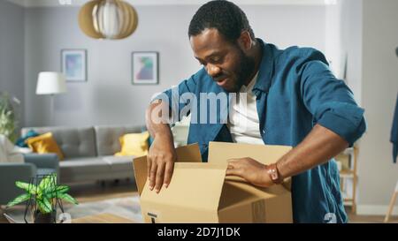 Bell'uomo eccitato apre cartone Box Postal Package ed è molto felice con il contenuto. Unboxing pacchetto uomo. Foto Stock