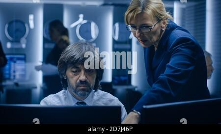 Il manager femminile parla con un operatore professionista che lavora su un personal computer nella sala di monitoraggio del sistema. Specialista di alto profilo che lavora. Foto Stock