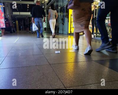 La gente cammina oltre una maschera medica scartata in un centro commerciale. Foto Stock