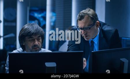 Il capo governativo della sicurezza informatica consulta il responsabile operativo che lavora sul computer. Specialisti che lavorano su computer nella sala di controllo del sistema. Foto Stock