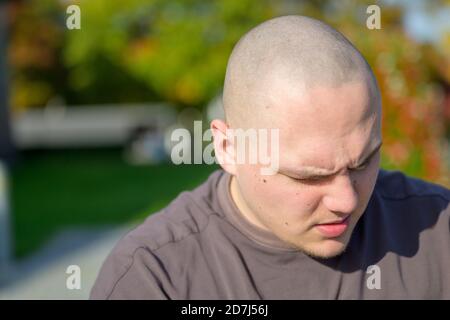 Giovane uomo con la testa rasata che guarda da vicino verticale su testa e spalle all'aperto Foto Stock