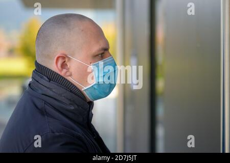 Profilo di un giovane che indossa una maschera protettiva Durante il Covid-19 o la pandemia del coronavirus circa entrare a. edificio in primo piano Foto Stock