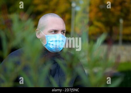 Nuovo stile di vita normale indossando una maschera per il viso all'aperto con un vista attraverso il verde di un giovane uomo nei suoi venti anni indossare una maschera chirurgica monouso Foto Stock