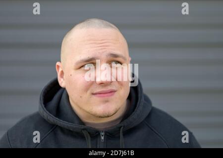 Giovane uomo con testina rasata che guarda in alto con un attento espressione e tranquillo accigliato mentre guarda qualcosa fuori schermo in un ritratto di primo piano Foto Stock