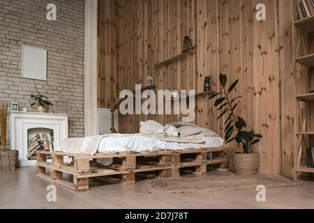 Accogliente camera da letto interna con camino bianco. Pareti con pannelli di legno e mattoni Foto Stock