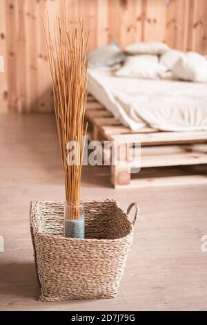 Decorazioni naturali in interni in legno della camera da letto. Bouquet di bastoni secchi in vaso e cesto di vimini al pavimento Foto Stock