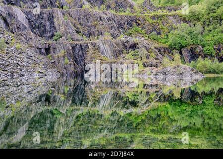 Scogliere d'ardesia che si riflettono in un lago limpido nelle Highlands scozzesi Foto Stock