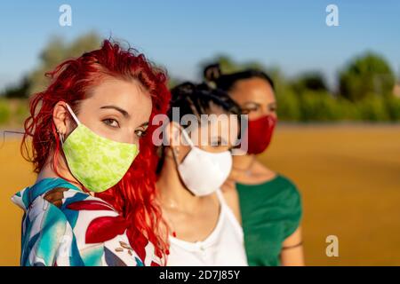 Gli amici indossano una maschera protettiva mentre si levano in piedi all'aperto al sole giorno Foto Stock