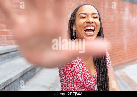 Donna che mostra un gesto di stop mentre si siede su una scala in città Foto Stock