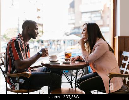 Sorridente giovane donna che parla con il ragazzo mentre si passa il tempo libero in caffetteria Foto Stock