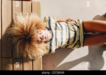 Donna con capelli biondi ricci con occhi chiusi reclinabili posto a sedere in legno durante la giornata di sole Foto Stock