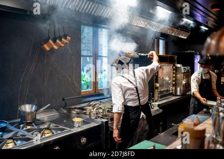 Gli chef indossano un piatto da cucina con maschera protettiva nella cucina del ristorante Foto Stock