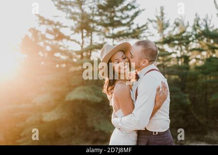 Coppia eterosessuale baciare mentre si trova in piedi nella foresta durante il tramonto Foto Stock