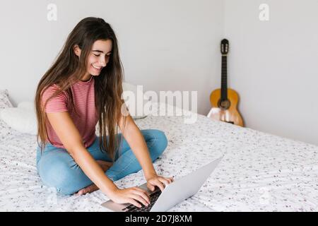 Giovane donna che usa il computer portatile mentre si siede a casa in camera da letto Foto Stock