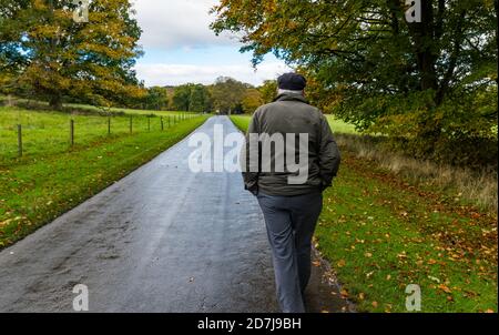 Dalmeny Estate, Edimburgo, Scozia, Regno Unito, 23 ottobre 2020. UK Weather: Una mattina nuvolosa umida non sminuisce i colorati alberi d'autunno come un uomo anziano che indossa un cappuccio piatto con le mani in tasche cammina su un sentiero pubblico Foto Stock